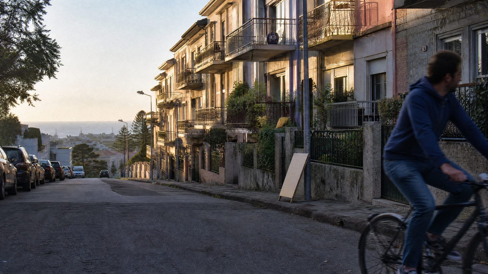 Rua residencial em Porto ao fim da tarde, com prédios de habitação e um letreiro de venda de casas ao fundo.
